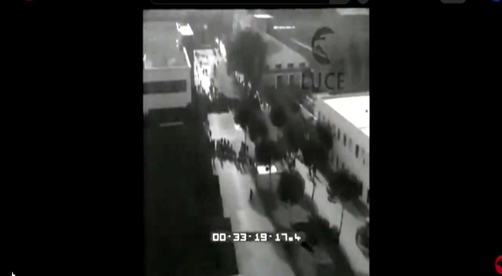 Vista aerea in bianco e nero di una strada affollata con persone e alberi lungo il percorso.